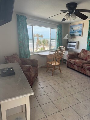 Ein Zimmer mit Esstisch, einer Couch, einem Sessel, einem Deckenventilator, einem Fenster mit Meerblick und einer Klimaanlage.