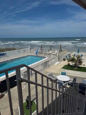 A pool area with a view of the ocean, lounge chairs, and a statue. - Room 19-Efficiency Unit-Ocean Front 1st floor (Daytona Beach)