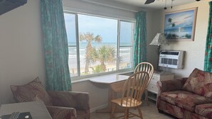 A room with a dining table, a sofa, a chair, a ceiling fan, a window with a view of the ocean, and an air conditioning unit. - Room 19-Efficiency Unit-Ocean Front 1st floor (Daytona Beach)