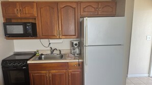 A compact kitchen with wooden cabinets, a microwave, a stove, a sink, and a refrigerator. - Room 19-Efficiency Unit-Ocean Front 1st floor (Daytona Beach)
