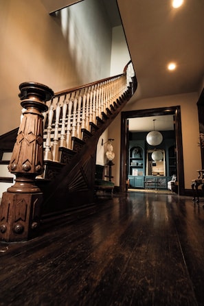 Eine prachtvolle Treppe mit hölzernem Geländer und Balustraden, die zu einem Raum mit einer Chandelier und Blick auf eine Stadtlandschaft führt.