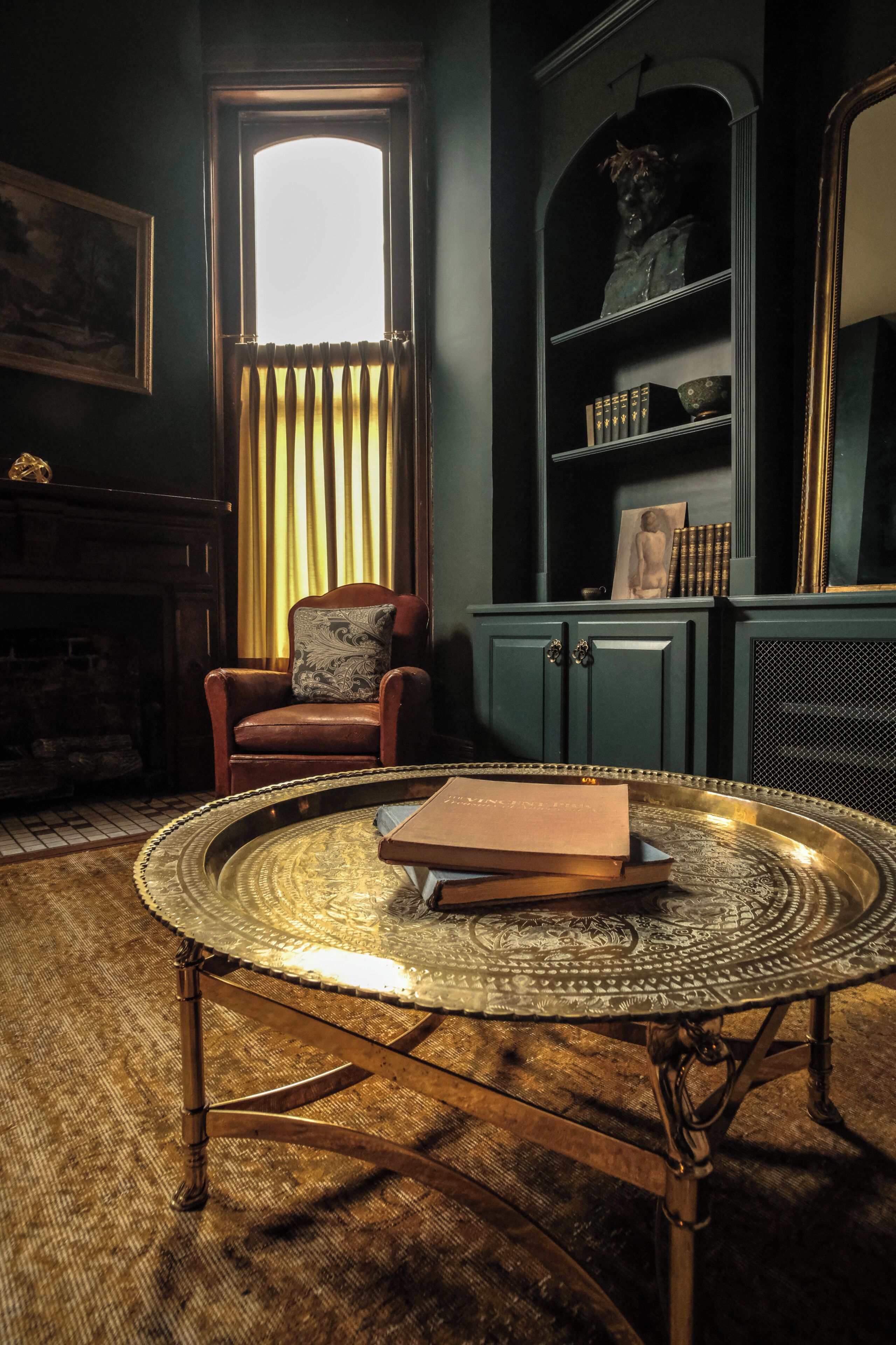 Una habitación con una mesa redonda de metal, un sillón de cuero, una estantería y una chimenea.