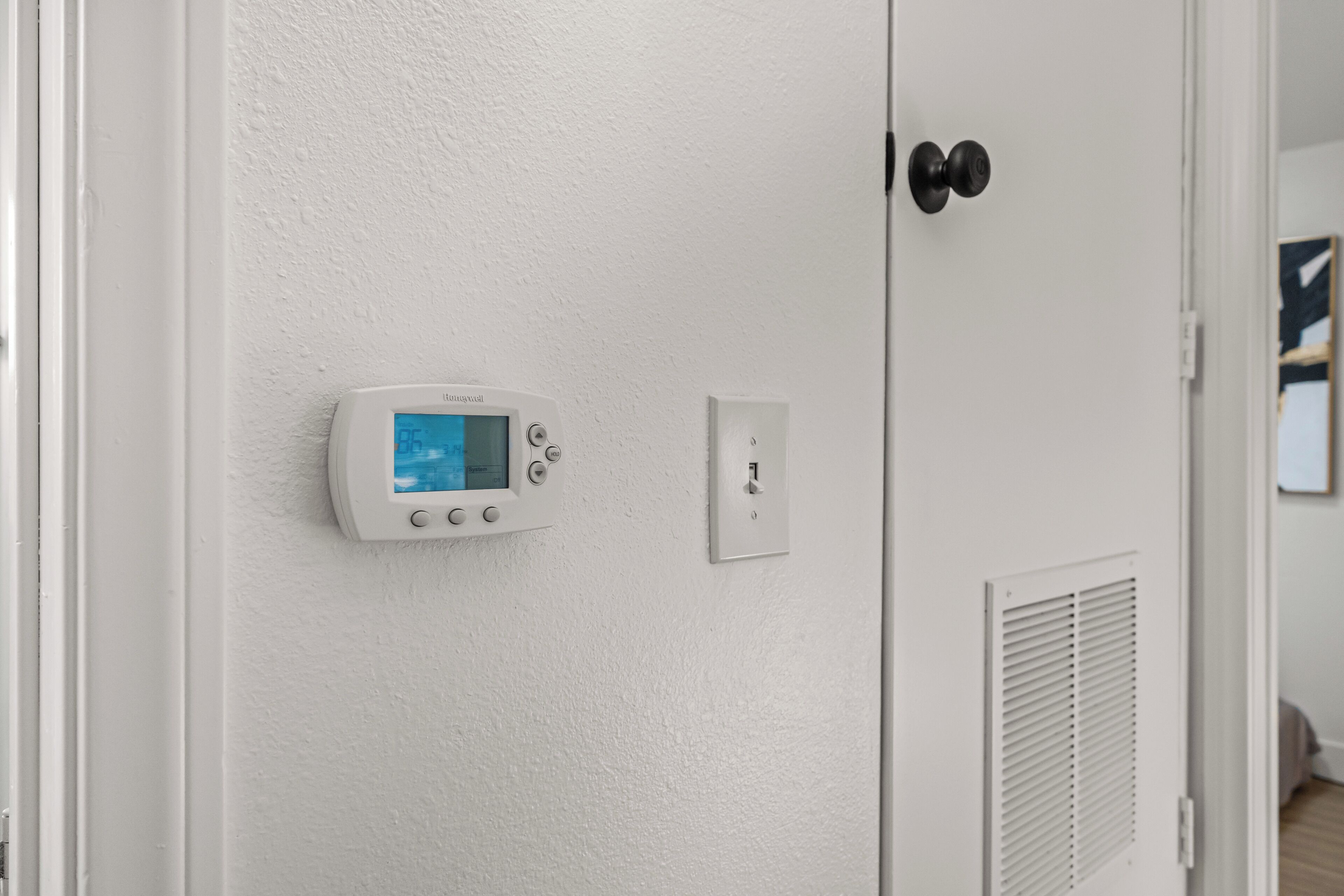 A thermostat mounted on a white wall, a door with a black handle, and a vent.