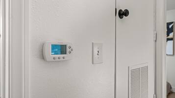 A thermostat mounted on a white wall, a door with a black handle, and a vent.