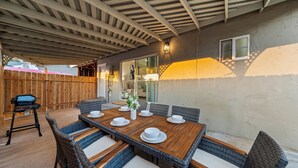 Une terrasse extérieure avec une table en bois dressée pour le repas, des chaises en osier et un barbecue.