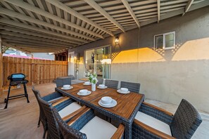 Eine Terrasse im Freien mit einem Holztisch, der für das Essen gedeckt ist, Korbstühlen und einem Grill.