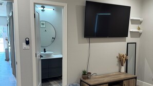 A bedroom with a bed, a TV mounted on the wall, a wooden console table, a mirror, and a bathroom visible through an open door.
