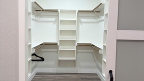 A walk-in closet with open doors, wooden flooring, and a black handle.