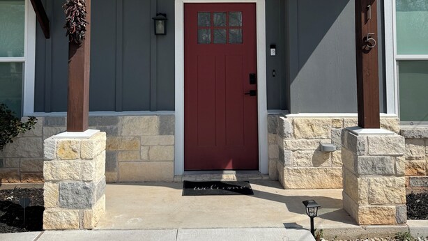A house with a red door, stone pillars, and a welcome mat.