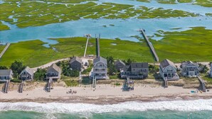 An aerial view of a coastal property with a beach, a pier, and a marshy area with water channels. - Beachfront Bliss with Marsh Views & Private Dock (East Sandwich)