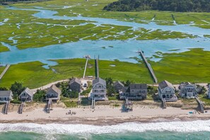 An aerial view of a coastal property with a beach, a pier, and a marshy area with water channels. - Beachfront Bliss with Marsh Views & Private Dock (East Sandwich)