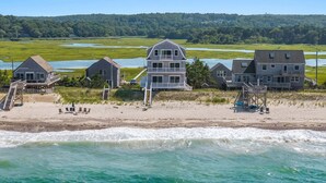 A beachfront property with multiple houses, a sandy beach, and a view of the ocean. - Beachfront Bliss with Marsh Views & Private Dock (East Sandwich)