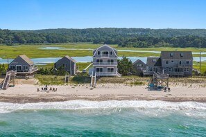 A beachfront property with multiple houses, a sandy beach, and a view of the ocean. - Beachfront Bliss with Marsh Views & Private Dock (East Sandwich)