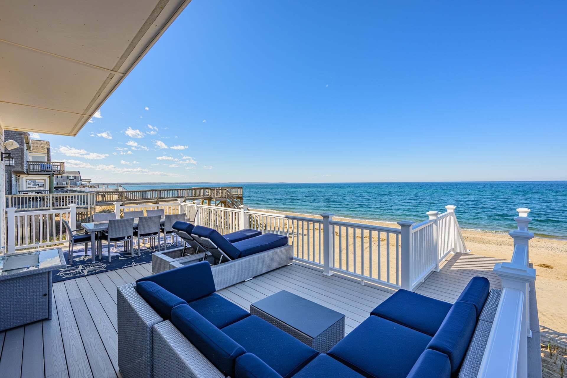 A deck with outdoor seating, a view of the ocean, and a wooden deck railing.