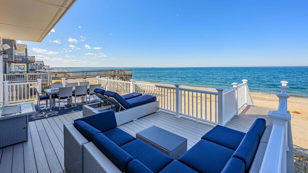 A deck with outdoor seating, a view of the ocean, and a wooden deck railing. - Beachfront Bliss with Marsh Views & Private Dock (East Sandwich)