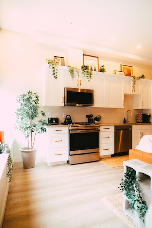 A modern kitchen with white cabinets, stainless steel appliances, and decorative plants. - Heritage 2BR w/ exposed brick & high ceilings (Halifax)