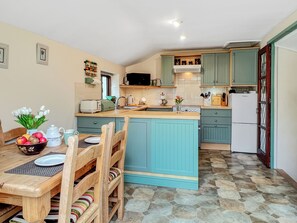 Una cocina compacta con armarios verde agua, una isla central, una mesa de comedor con sillas y un refrigerador.