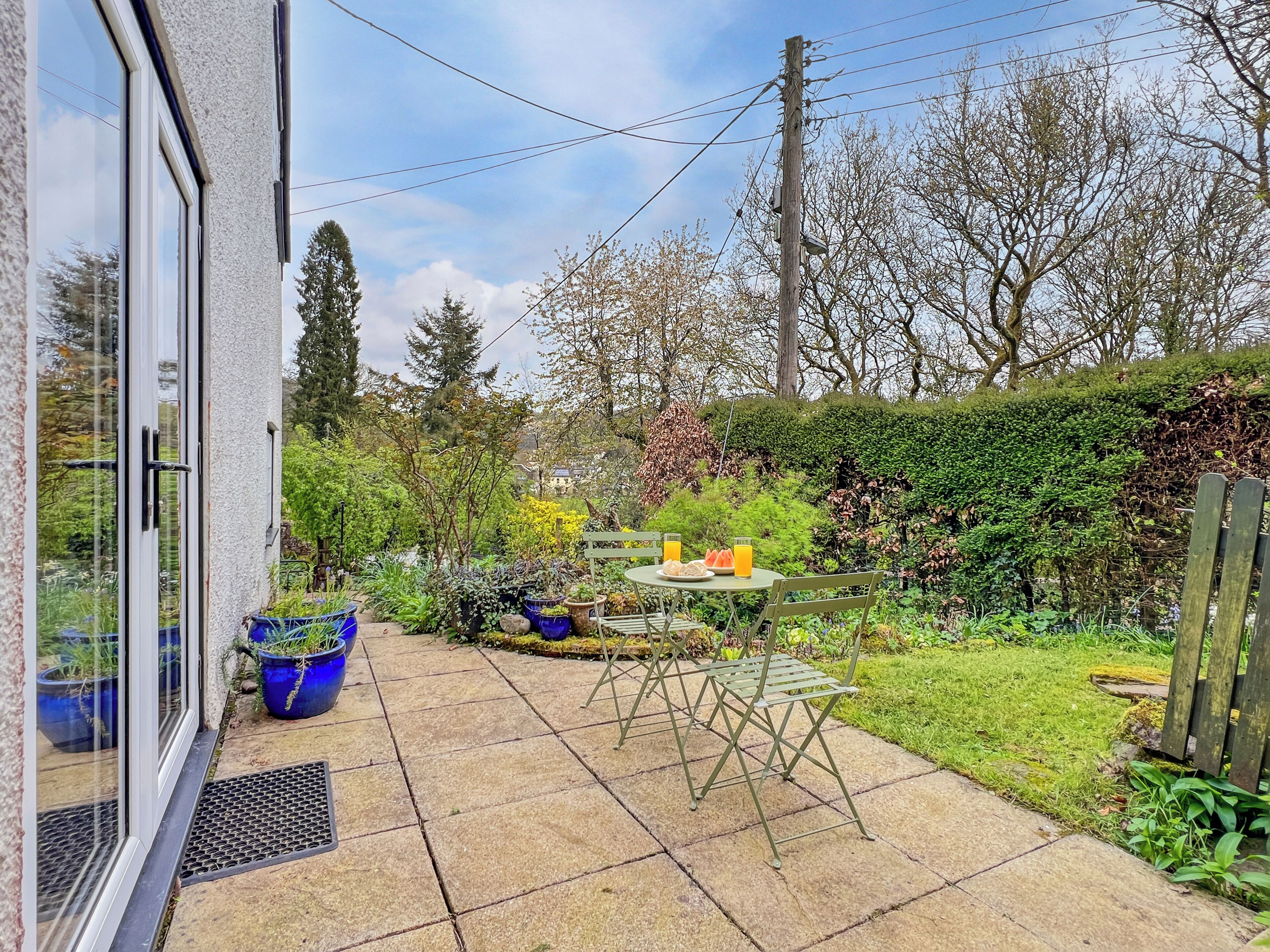 Une terrasse avec une table et des chaises, entourée de plantes en pot et d’une pelouse.
