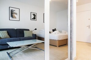 Ein modernes Zimmer mit einer Couch, einem kleinen Tisch, einem Bett und zwei gerahmten Kunstwerken an der Wand.