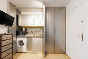 Eine kleine Küche mit Waschmaschine, Kaffeemaschine und einem Fernseher auf einem Schrank.