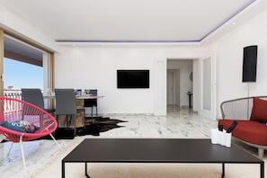 Ein modernes Wohnzimmer mit Essbereich, einem Flachbildfernseher, einer Couch und einem roten Sessel.