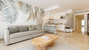 A modern living room with a sofa, a round bamboo coffee table, and a kitchen area with a microwave and bar stools. - Upstays Elegant 1BR Gray d'Albion 2min from Palais (Cannes)
