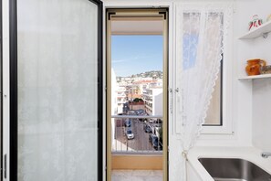 A room with a balcony, a view of a street, and a kitchen area. - Upstays  Sea View 25m² Studio Moure Rouge (Cannes)