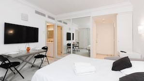 Habitación de hotel con cama, escritorio, silla, televisión y baño visible a través de una puerta abierta.