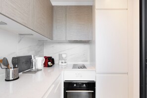 A modern kitchen with a built-in oven, a coffee maker, and a kettle on the counter. - Upstays  Sea View 25m² Studio Moure Rouge (Cannes)