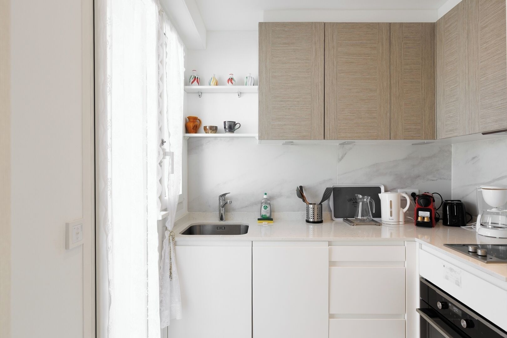 A modern kitchen with white cabinetry, a stainless steel sink, and a coffee maker.