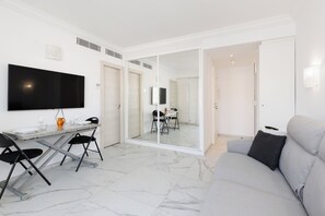 A modern living room with a sofa, a dining table with chairs, a flat-screen TV, and a sliding glass door leading to another room. - Upstays  Sea View 25m² Studio Moure Rouge (Cannes)