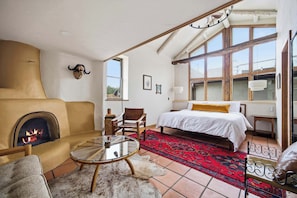 A room with a fireplace, a bed, a sofa, a glass table, and a red patterned rug.