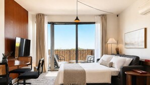 A hotel room with a bed, a desk with a TV, a dining area, and a balcony with a view. - Bay View Designer 2BR · Best Location with Balcony, Gym, and Terrace · Sleeps 6 (Milwaukee)