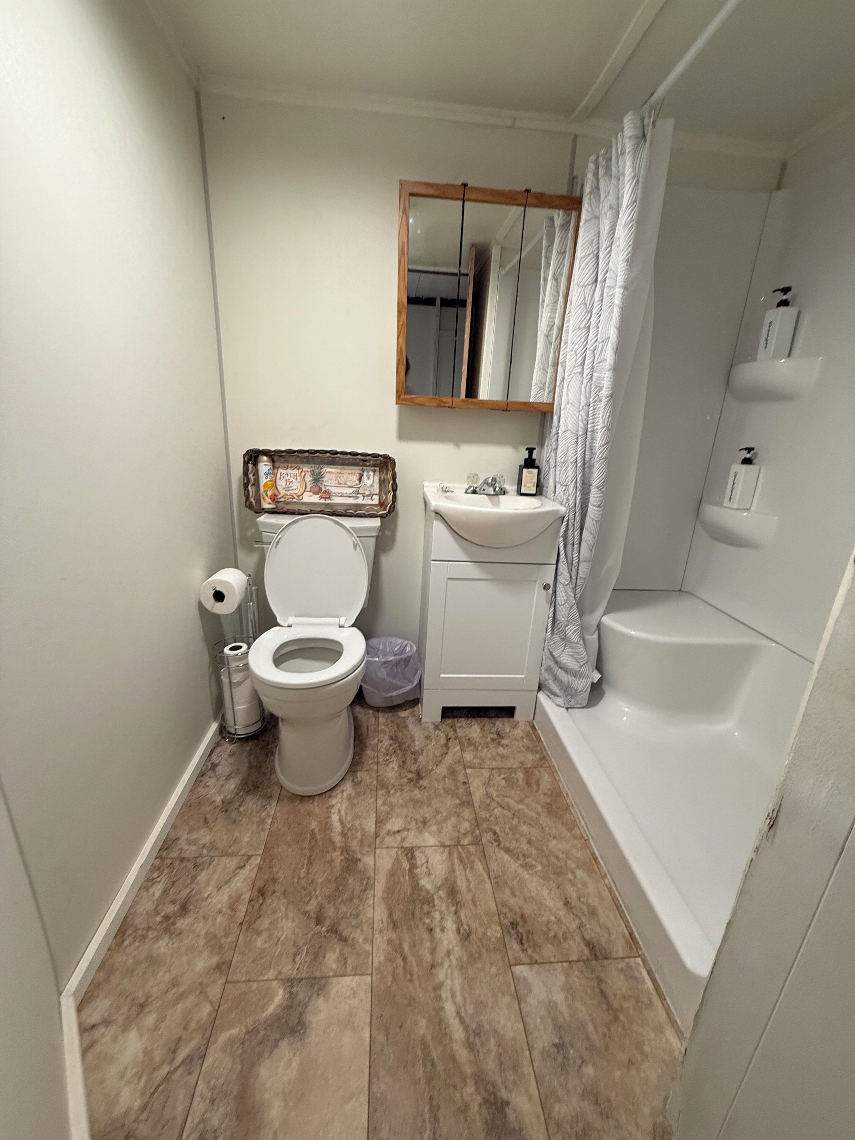 A bathroom with a toilet, sink, mirror, shower curtain, and a decorative frame on the wall.