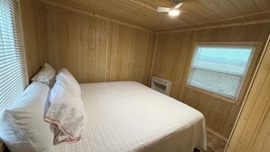 A wooden-paneled room with a bed, a ceiling fan, and a window with blinds.