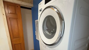 A laundry room with stacked washers and dryers, a wooden door, and a blue wall.
