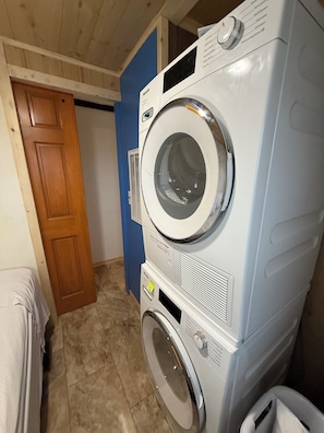 A laundry room with stacked washers and dryers, a wooden door, and a blue wall.