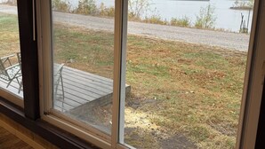 A view through a window of a deck area with a gravel path and a body of water in the background.