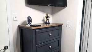 Een kamer met een zwarte dressoir, een tv aan de muur en een beerbeeldje.