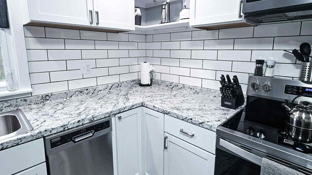 Een moderne keuken met witte kastjes, een RVS vaatwasser, een fornuis en een magnetron.