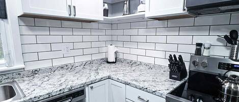 A modern kitchen with white cabinets, a stainless steel dishwasher, a stove, and a microwave.