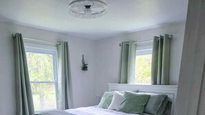 Een slaapkamer met een bed, nachtkastje, kaptafel en een raam met gordijnen.