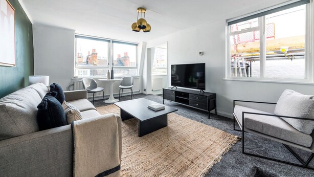 Ett modernt vardagsrum med en soffa, ett soffbord, en tv och stora fönster som erbjuder utsikt över stadsbilden.