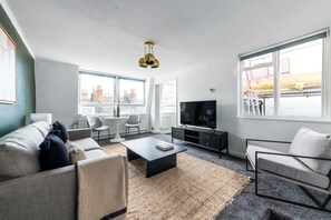 Una sala de estar moderna con sofá, mesa de centro, televisor y ventanas amplias que dan a vistas de la ciudad.