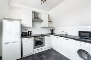 Eine moderne Küche mit weißen Schränken, einem Geschirrspüler, einem Backofen, einer Mikrowelle und einer Waschmaschine.
