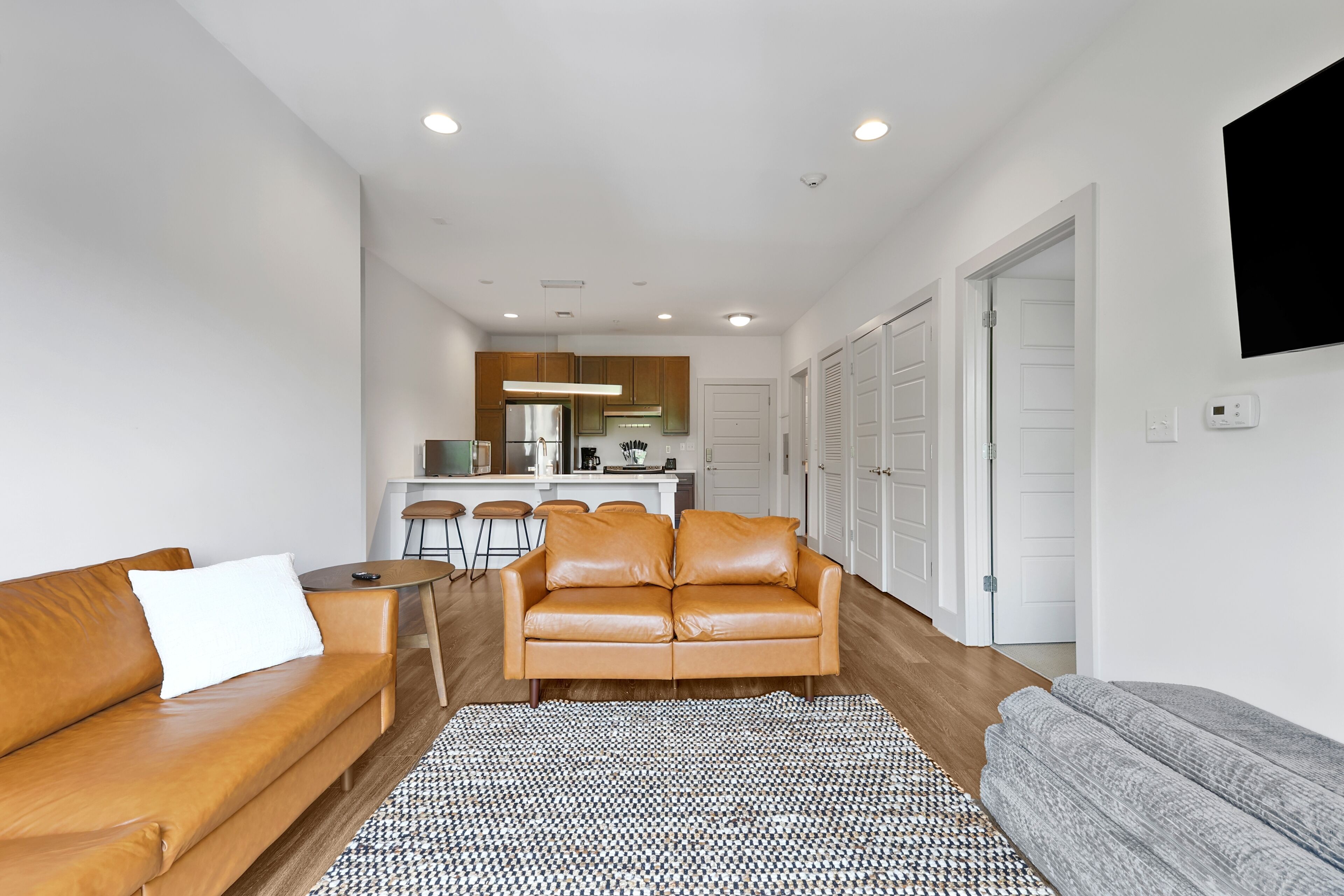 A modern living room with a leather sofa, a patterned rug, and a kitchen in the background.