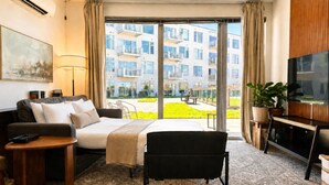 Habitación de hotel con cama, sofá, televisor, escritorio y ventana grande con vista a un edificio.