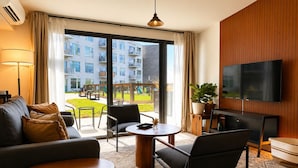 Habitación de hotel moderna con sofá, sillas, televisor y un amplio ventanal con vistas al exterior del edificio.