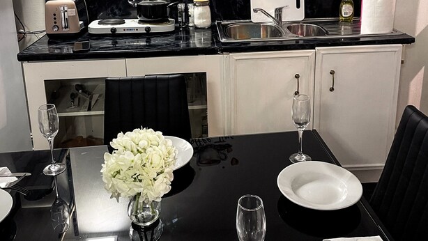 A modern kitchen with a coffee-themed wall art, a dining table set with plates, glasses, and a vase of flowers. - Large StudioFlat in heart of Camden market (London)