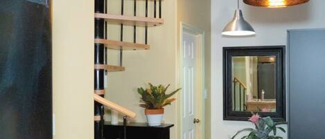 Una cocina con un lavamanos de acero inoxidable, escalera de madera, plantas en macetas e iluminación colgante.